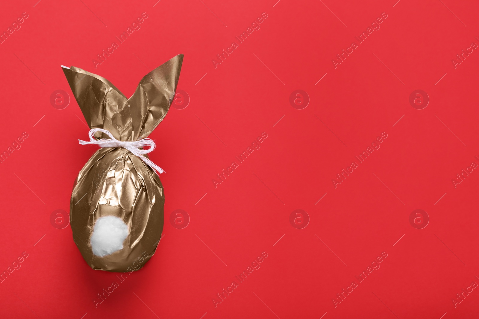 Photo of Easter bunny made of shiny gold paper on red background, top view. Space for text