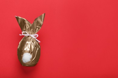 Easter bunny made of shiny gold paper on red background, top view. Space for text