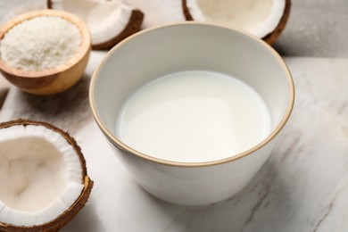 Photo of Bowl of delicious coconut milk, flakes and coconuts on white table