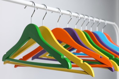 Photo of Bright clothes hangers on metal rack against light background, closeup