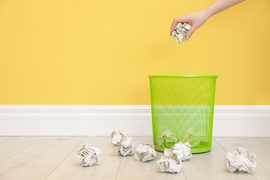 Photo of Woman throwing crumpled paper into metal bin against color wall. Space for text