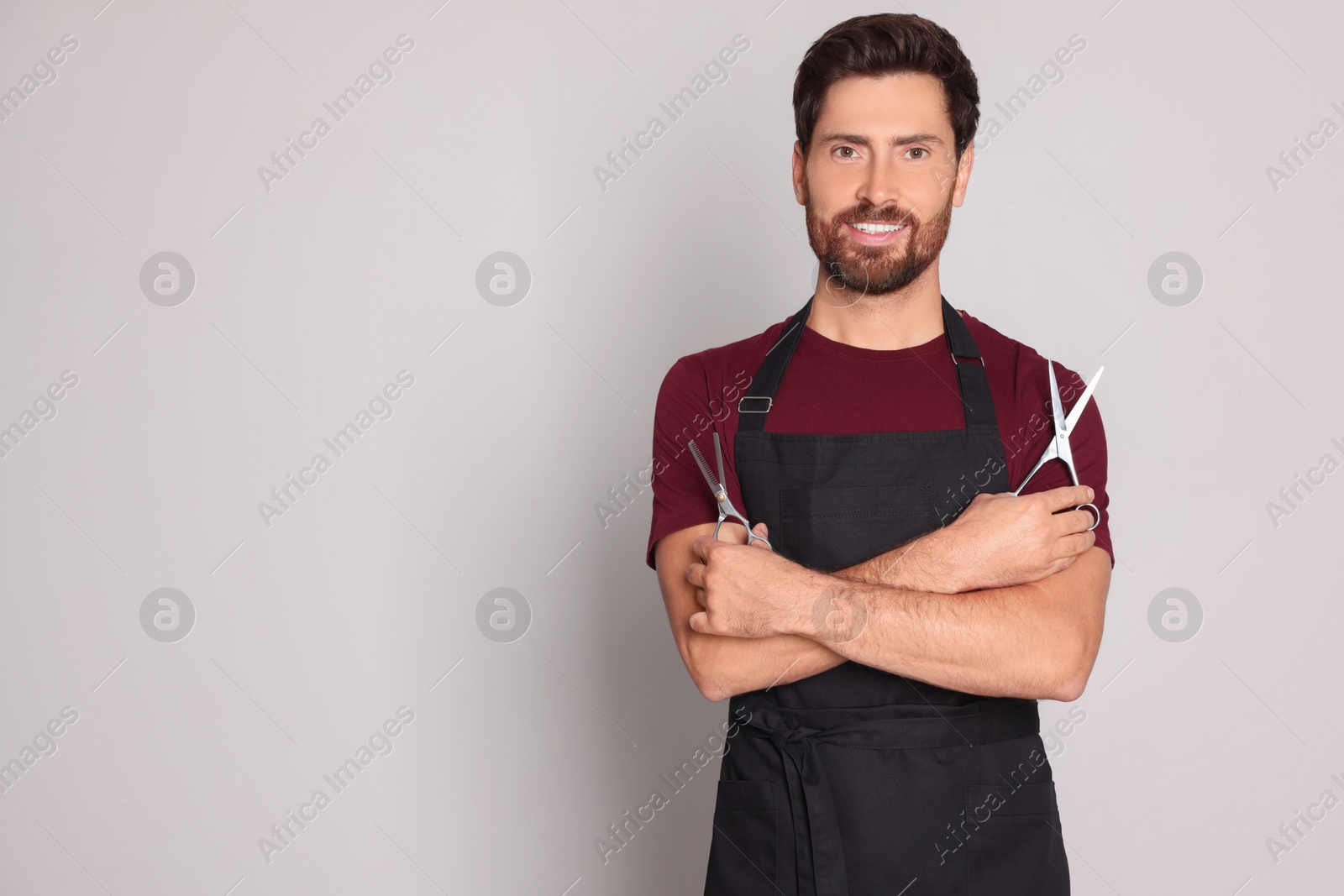 Photo of Smiling hairdresser with scissors on light grey background, space for text