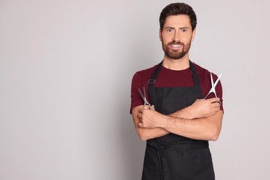 Smiling hairdresser with scissors on light grey background, space for text