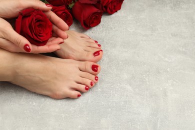Photo of Woman with stylish red toenails after pedicure procedure and rose flowers on grey textured floor, top view. Space for text