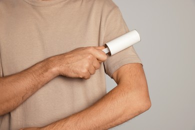 Man using lint roller on light grey background, closeup