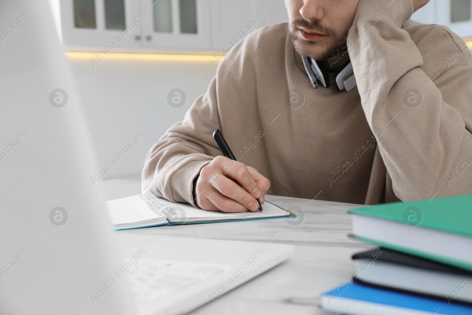 Photo of Young man using modern laptop for studying in kitchen, closeup. Distance learning