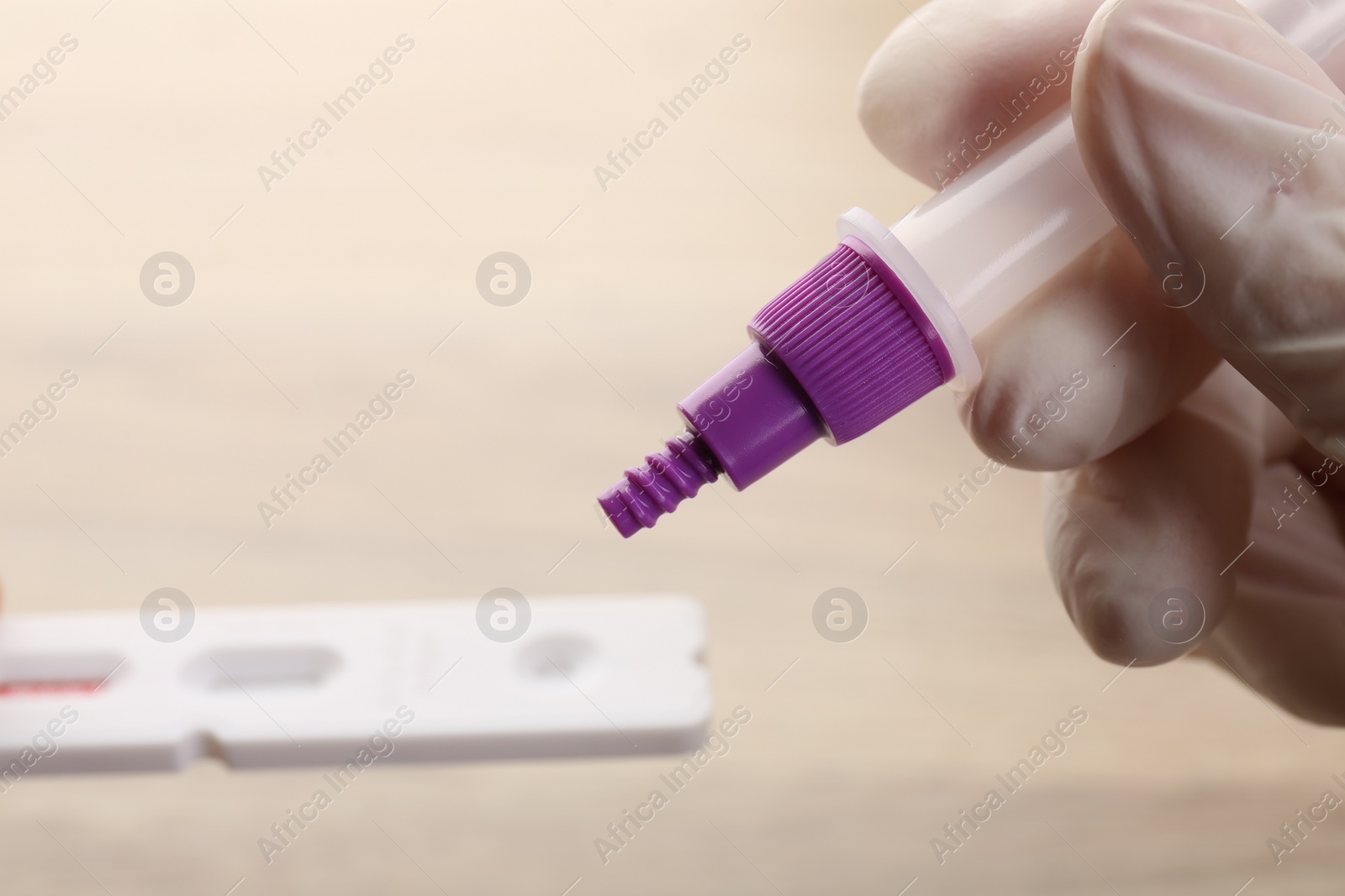 Photo of Doctor dropping buffer solution onto disposable express test cassette against blurred background, closeup