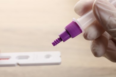 Doctor dropping buffer solution onto disposable express test cassette against blurred background, closeup