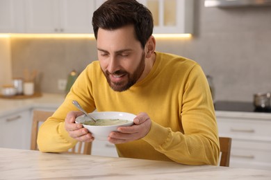 Photo of Man enjoying delicious soup at light marble table in kitchen