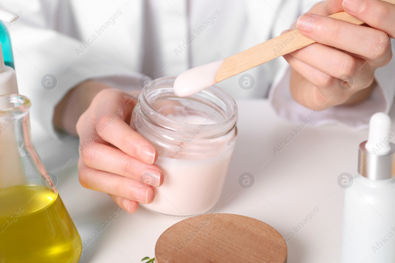 Photo of Dermatologist with jar testing cosmetic product at white table, selective focus