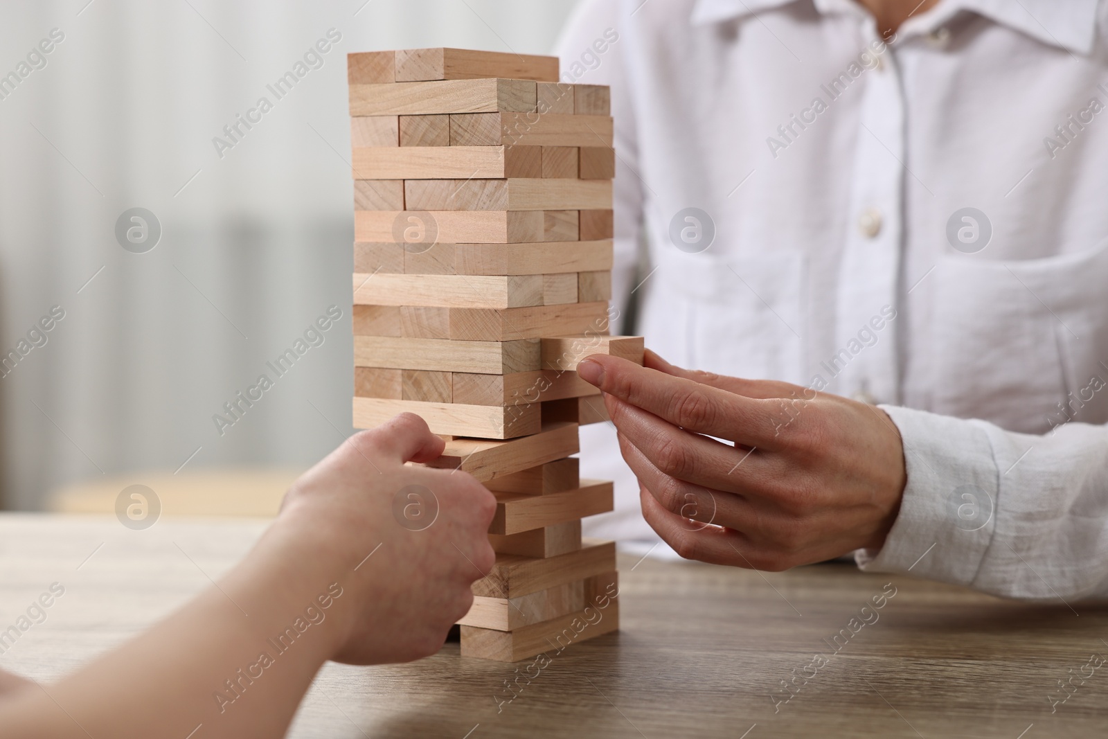 Photo of People playing Jenga tower at wooden table indoors, closeup