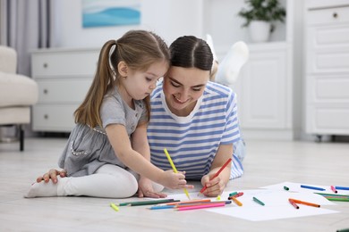 Mother and her little daughter drawing with colorful markers on floor at home