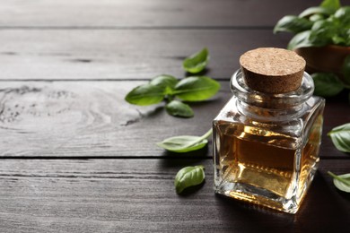 Photo of Glass bottle of basil essential oil and leaves on wooden table. Space for text