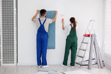 Workers hanging light blue wallpaper in room