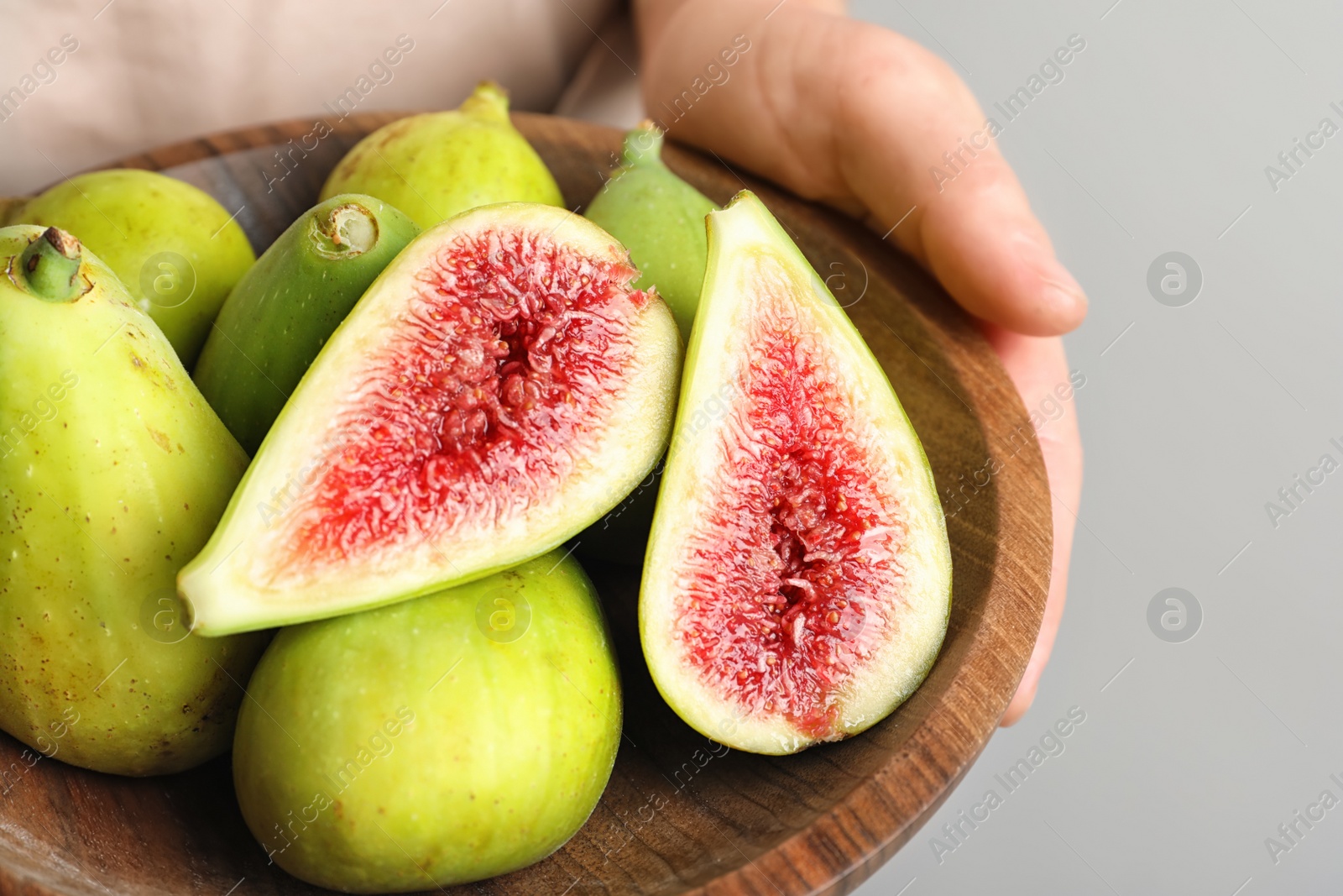 Photo of Woman holding bowl with fresh ripe figs on light background