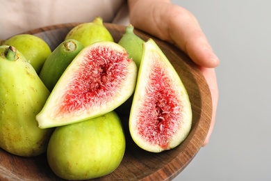 Woman holding bowl with fresh ripe figs on light background