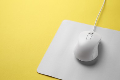 Wired mouse with mousepad on yellow background, closeup. Space for text