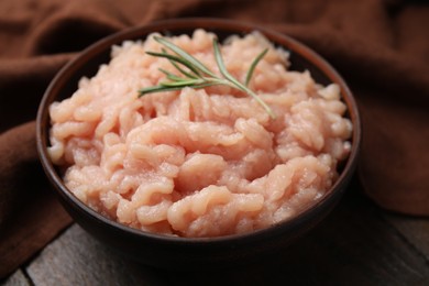 Fresh raw minced meat and rosemary in bowl on wooden table, closeup