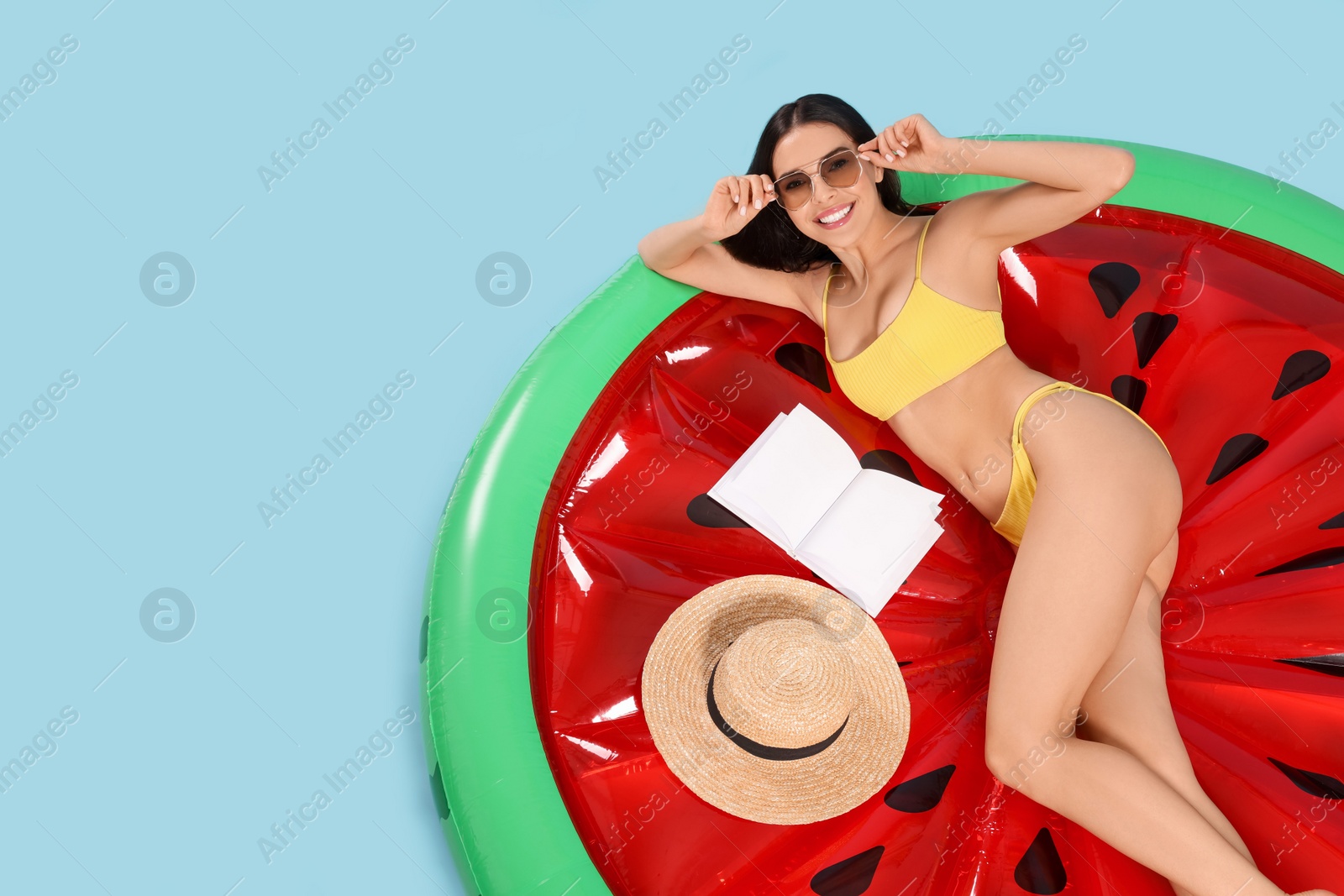 Photo of Young woman with book on inflatable mattress against light blue background