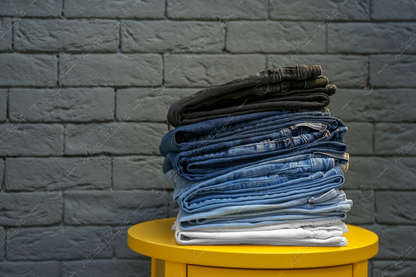 Photo of Stack of different jeans on table against brick wall