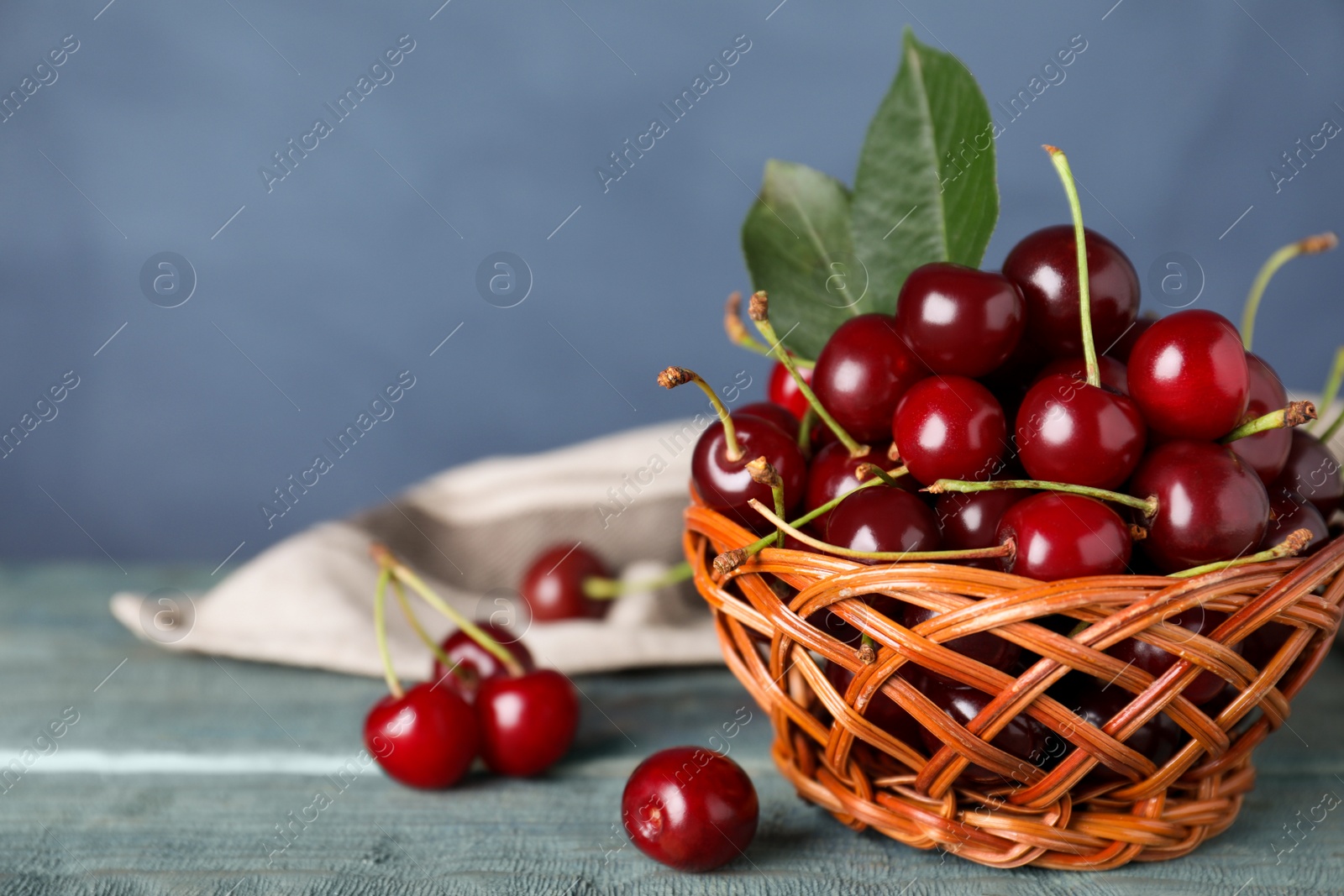 Photo of Sweet juicy cherries with leaves on wooden table against blue background, closeup. Space for text