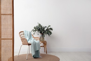 Photo of Stylish wooden chair, folding screen and beautiful bunch of eucalyptus branches in room