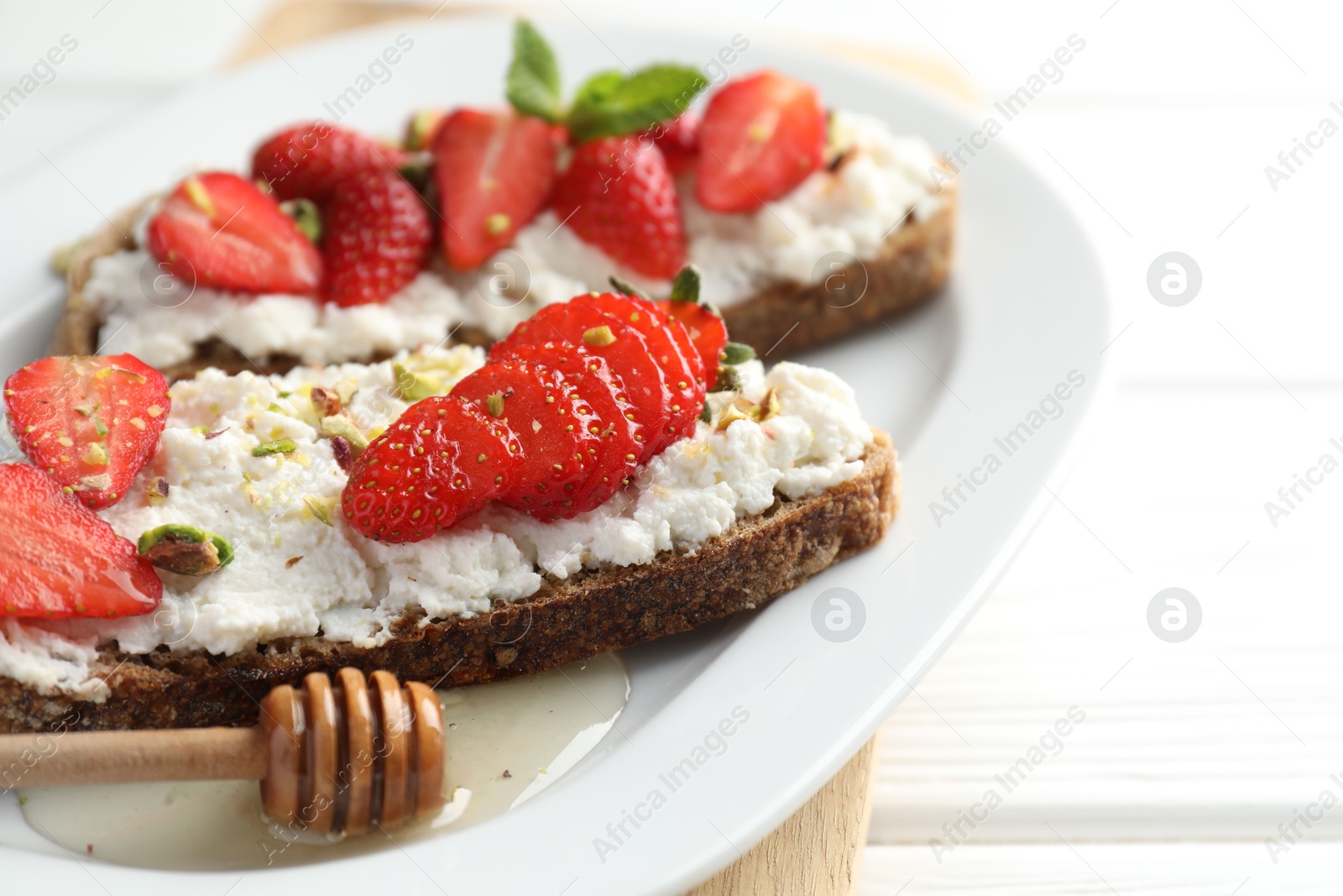 Photo of Delicious ricotta bruschettas with strawberry and pistachios served with honey on white table, closeup