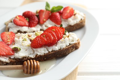 Photo of Delicious ricotta bruschettas with strawberry and pistachios served with honey on white table, closeup