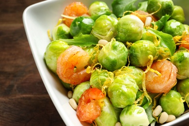 Photo of Bowl of delicious salad with Brussels sprouts and shrimps on table, closeup