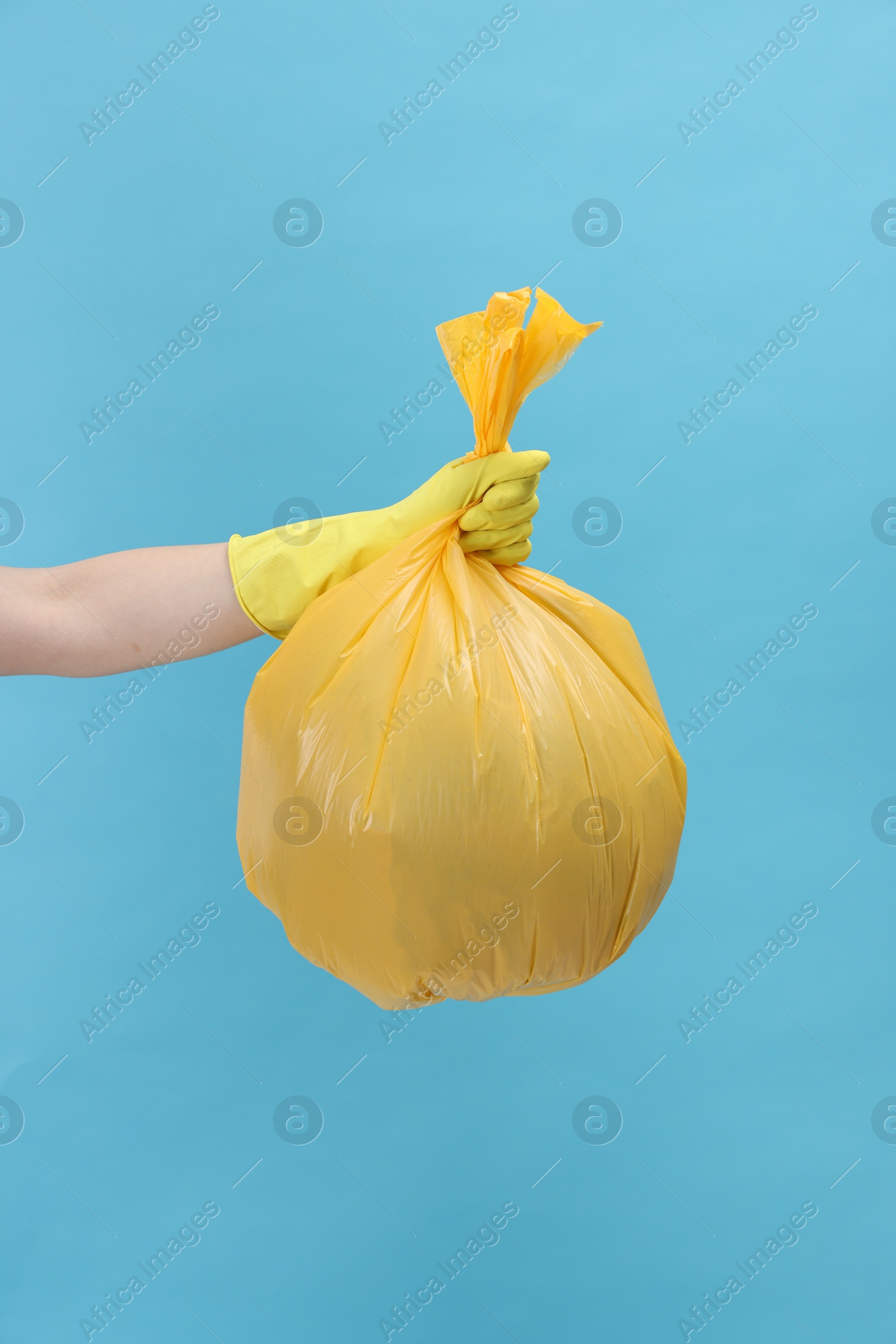 Photo of Woman holding plastic bag full of garbage on light blue background, closeup