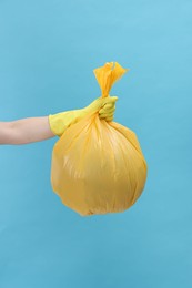 Woman holding plastic bag full of garbage on light blue background, closeup