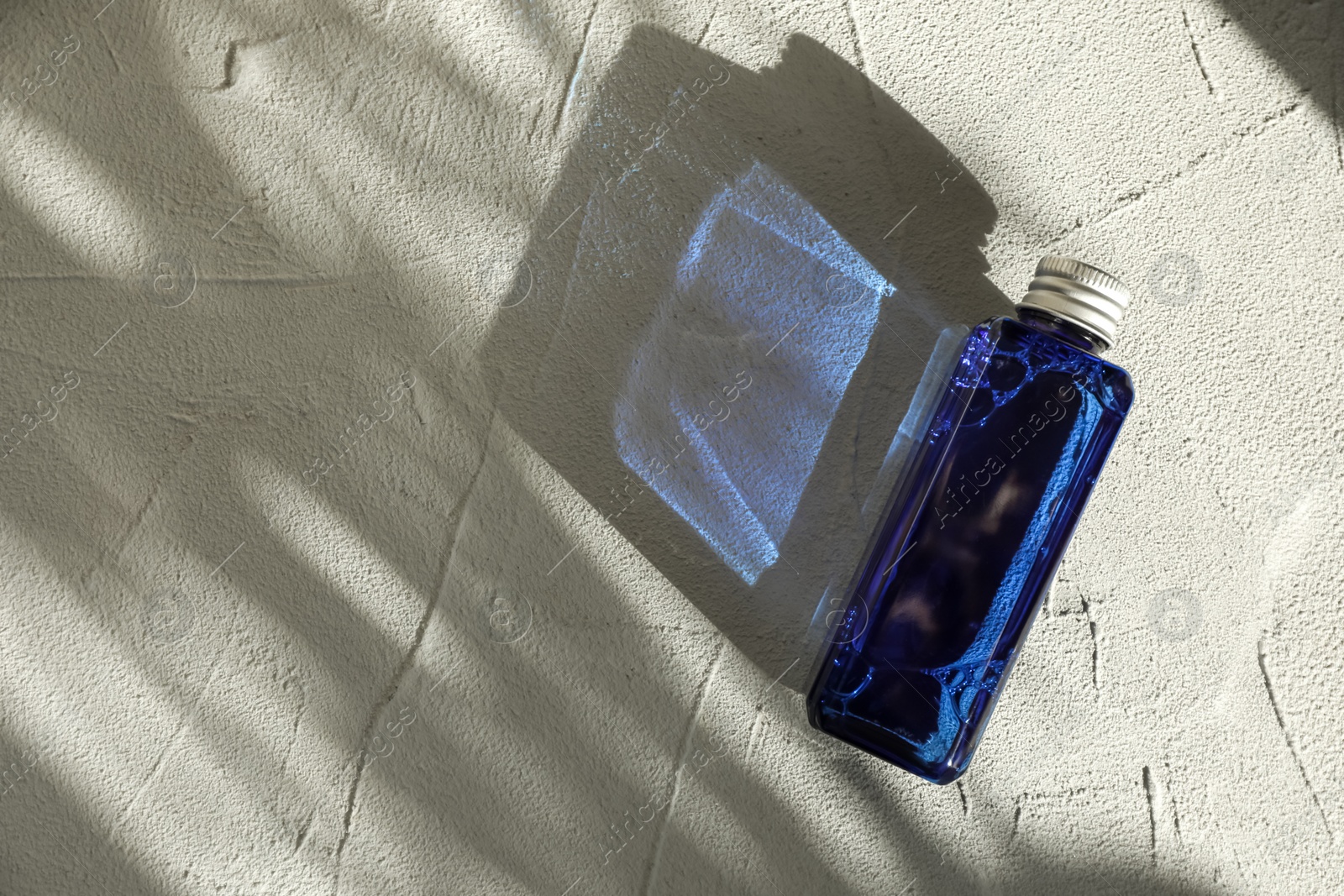 Photo of Cosmetic product in blue bottle on light textured background, top view. Space for text