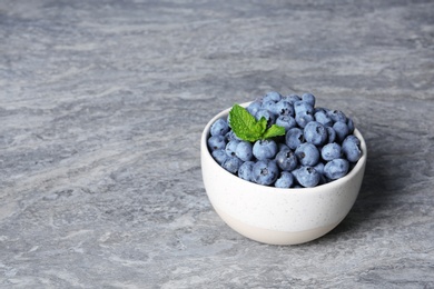 Photo of Bowl with fresh blueberries and green leaves on table. Space for text