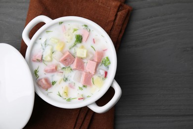 Photo of Delicious cold summer soup (okroshka) with boiled sausage in pot on grey wooden table, top view. Space for text