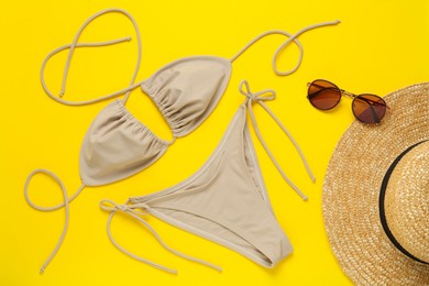 Photo of Stylish beige bikini, sunglasses and hat on yellow background, flat lay