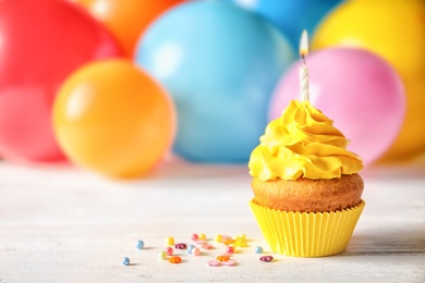 Delicious birthday cupcake with candle and blurred balloons on background