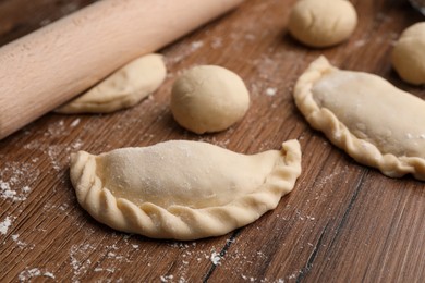 Photo of Uncooked chebureki, dough and rolling pin on wooden table