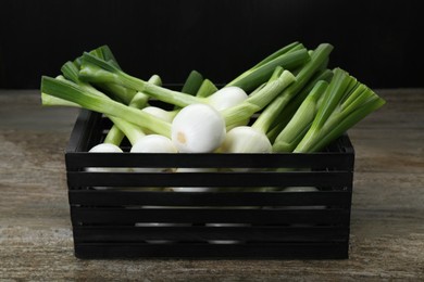 Photo of Black crate with green spring onions on wooden table