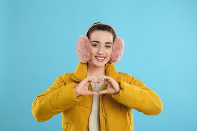 Photo of Beautiful young woman wearing earmuffs on light blue background