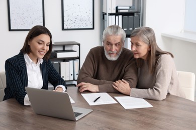 Elderly couple consulting insurance agent about pension plan at wooden table indoors
