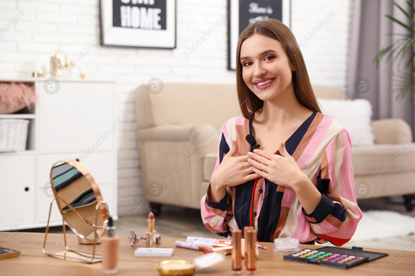 Photo of Beauty blogger at table with different cosmetic products indoors