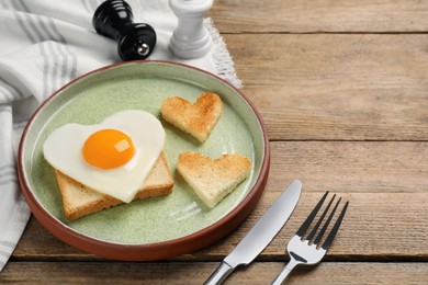 Photo of Heart shaped fried egg with toasts served on wooden table. Space for text