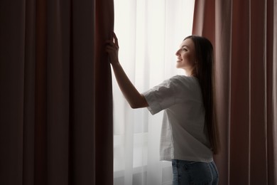 Happy woman opening stylish window curtains at home