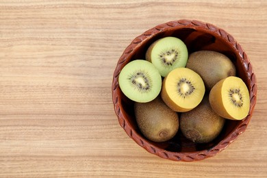 Photo of Bowl of many whole and cut fresh kiwis on wooden table, top view. Space for text