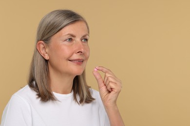 Photo of Senior woman taking pill on beige background. Space for text