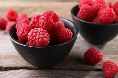 Photo of Tasty ripe raspberries in bowls on wooden table, closeup