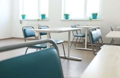 Photo of Empty school classroom with desks, windows and chairs