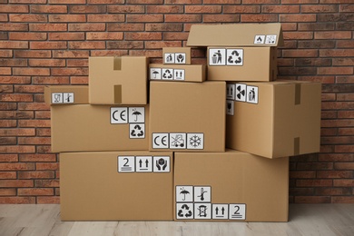Photo of Cardboard boxes with different packaging symbols on floor near brick wall. Parcel delivery