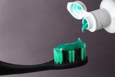 Photo of Applying paste on toothbrush against grey background, closeup