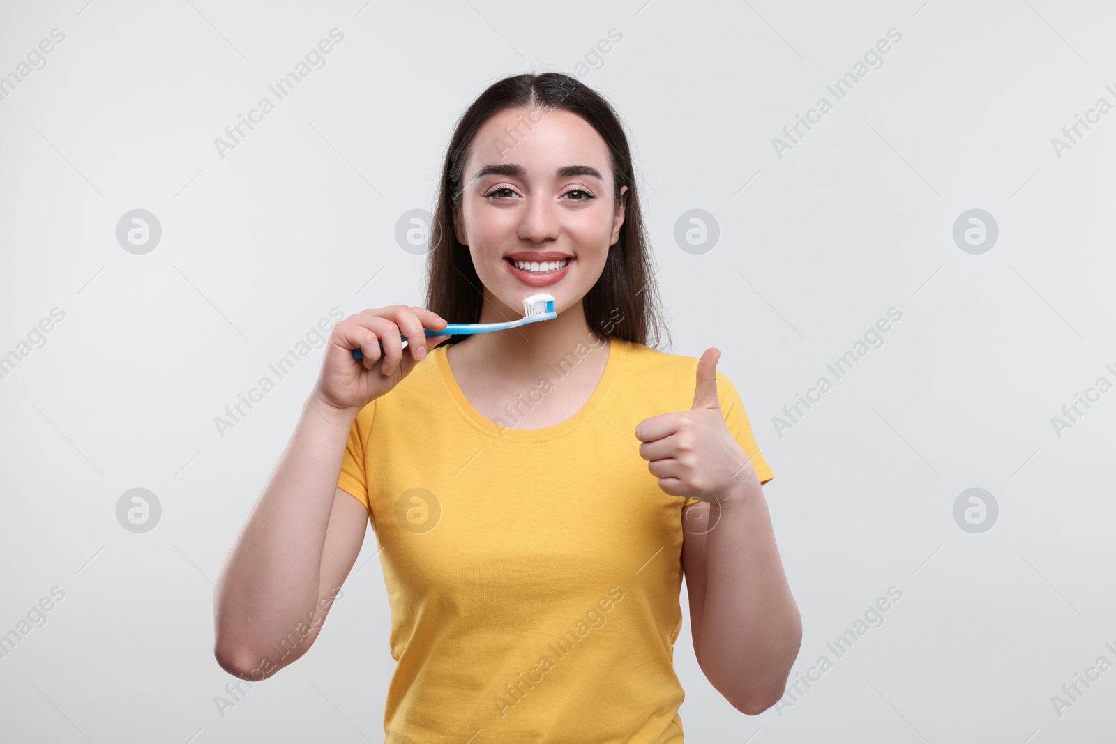 Photo of Happy young woman holding plastic toothbrush and showing thumb up on white background